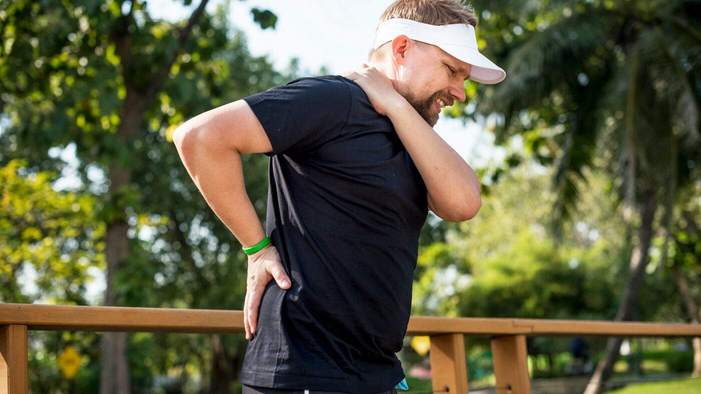A man outdoors holding his lower back in pain from a bulging disc